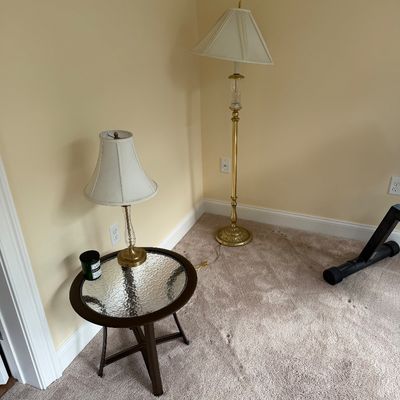 Traditional brass floor lamp and matching table lamp with cream shades, paired with a round dark wood side table featuring a textured...