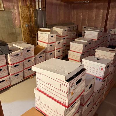 Numerous stacks of numbered white cardboard banker boxes filled with items, stored in an unfinished basement with exposed insulation.
