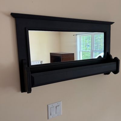 Wall-mounted black wooden mirror featuring a built-in display shelf below the glass.
