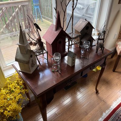Queen Anne style cherry console table displaying a collection of decorative wooden birdhouses and rustic branch accents.