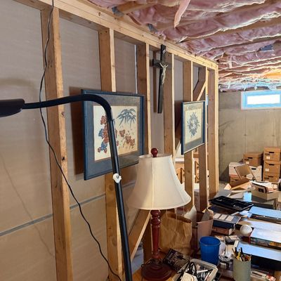 Unfinished basement storage area featuring framed Asian-style artwork, a wooden crucifix, a red table lamp, and various office supplies...