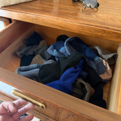 Mid-century modern wooden dresser drawer with a brass pull handle, shown open and containing various socks.