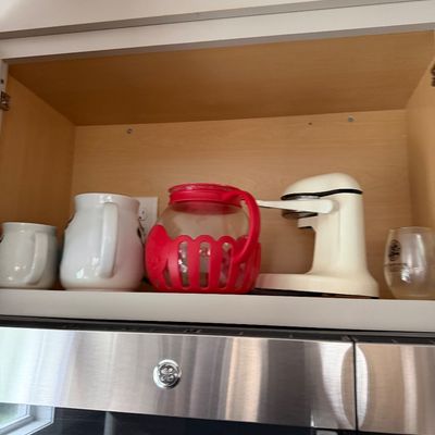 Assorted kitchenware stored in a cabinet, including a red-accented glass pitcher, a white ceramic pitcher, and a vintage-style...