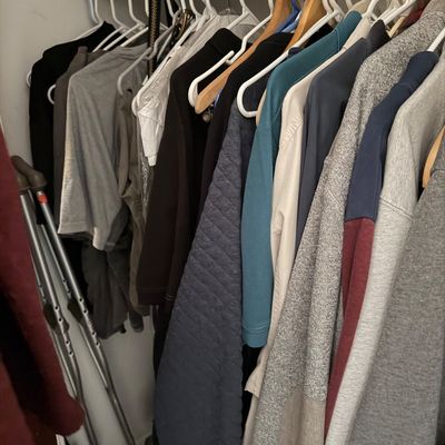 Assorted men's clothing including shirts, sweaters, and jackets hanging in a closet, alongside a pair of metal crutches.