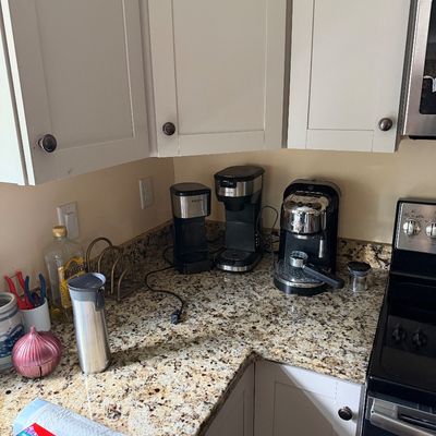 Collection of kitchen countertop appliances, including a Krups coffee maker, a drip coffee machine, and a De'Longhi espresso maker,...