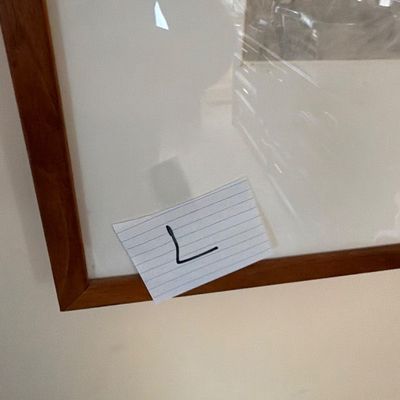 Framed artwork with a wooden frame and white matting, featuring a handwritten label marked with the letter 'L'.