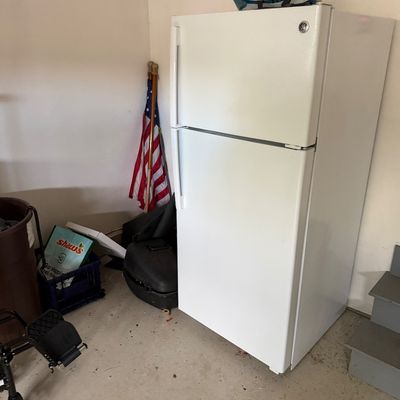 White GE top-freezer refrigerator, showing some light exterior wear, situated in a garage setting.