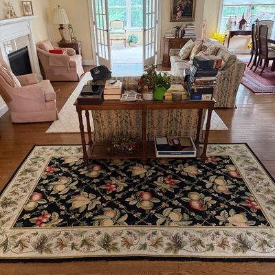Traditional area rug featuring a botanical fruit and vine pattern on a black field with a cream border, shown in a living room setting.