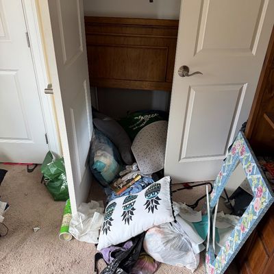 Assorted household items including a floral-painted mirror frame, decorative pineapple pillow, and various linens piled near a closet.