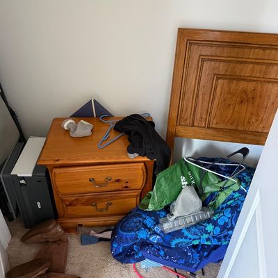 Two-drawer pine nightstand with brass pulls, shown alongside a matching wooden headboard and various household items.
