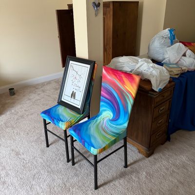 Pair of metal-framed dining chairs fitted with vibrant, multi-colored swirl pattern fabric slipcovers.