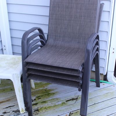 Stack of four contemporary outdoor patio armchairs with dark metal frames and brown woven mesh seats.