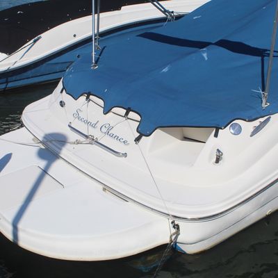Stern view of a white motorboat named 'Second Chance' fitted with a blue canvas cover, docked in a slip.