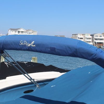 Sea Ray boat featuring a folded blue bimini top with cover, attached stainless steel frame, and matching blue mooring cover.