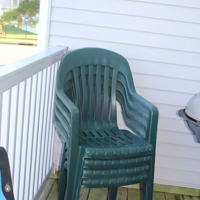 Stack of four hunter green resin patio lawn chairs sitting on an outdoor wooden deck.