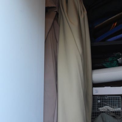 Pair of large beige and taupe patio umbrellas stored vertically in a closet alongside various outdoor and household items.
