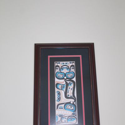 Framed Pacific Northwest Indigenous-style artwork featuring stylized formline motifs in blue, black, red, and white. The piece is set in...