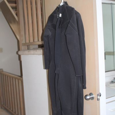 Full-body black neoprene wetsuit hanging from a door hook, featuring long sleeves and exposed seam stitching.