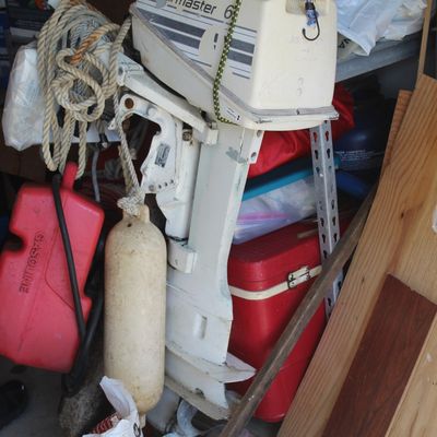 Vintage Sail Master 6 outboard boat motor stored alongside boating accessories including a buoy, rope, gas can, and a red cooler.