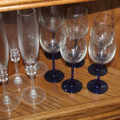 Assortment of glassware displayed inside a wooden corner cabinet, including clear crystal champagne flutes and textured wine glasses with...