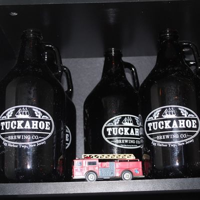 Collection of brown glass Tuckahoe Brewing Co. growlers alongside a small die-cast toy fire truck on a black shelf.