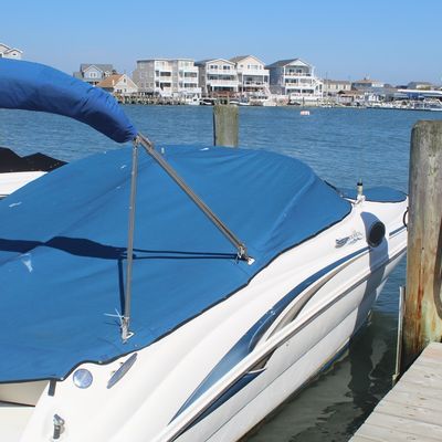 Sea Ray Sundeck motorboat fitted with a blue canvas fitted cover and matching bimini top, docked in a marina.