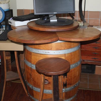 Rustic wood wine barrel desk with an expanded cloverleaf-shaped tabletop, featuring a matching stool and computer accessories set up on top.