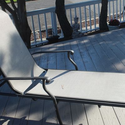 Modern outdoor lounge chair featuring a dark metal frame and light grey mesh sling seating, situated on a wooden deck.
