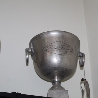 French-style metal champagne ice bucket branded 'Château St. Lemoine' alongside a carved wooden figurine.