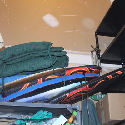 Assorted patio items including a folded outdoor umbrella, green seat cushions, and colorful bodyboards stored on utility shelving.