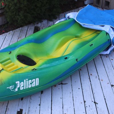 Pelican sit-on-top kayak in green, yellow, and blue swirl color scheme, shown with a partial blue storage cover.