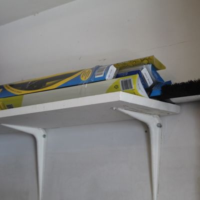 Assorted windshield wiper blades in original packaging stored on a white wall shelf alongside cleaning tools.
