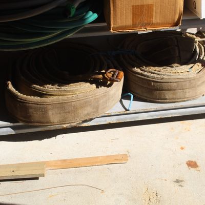 Two rolls of vintage heavy-duty canvas fire hose sitting on a metal utility shelf alongside garden hoses.