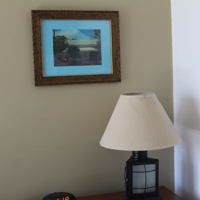 Framed tropical landscape print with light blue matting in an ornate gilded wood frame, displayed above a lantern-style table lamp.