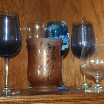 Collection of assorted glassware inside a wooden cabinet, including cobalt blue stemware, a frosted copper-toned votive holder, and clear...
