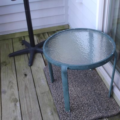 Round outdoor patio side table with a dark green metal frame and textured glass top.