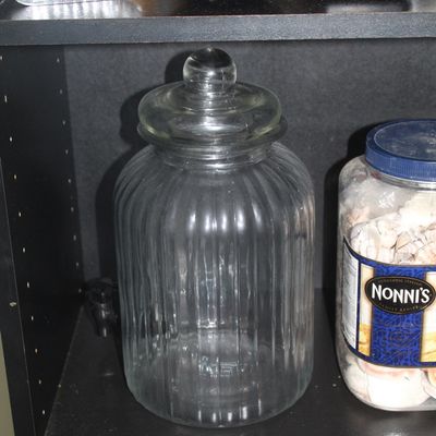 Large clear glass ribbed cookie jar with a round glass finial lid, displayed on a shelf.