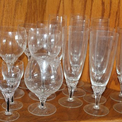 Collection of crystal stemware including wine glasses, champagne flutes, and a snifter on a wooden shelf.
