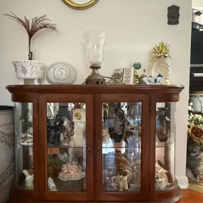 Traditional oak curio cabinet with curved glass sides, glass shelves, and double doors, filled with various figurines and collectibles.
