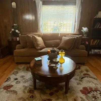 Traditional brown upholstered sofa with matching throw pillows, paired with a round wooden coffee table on a floral patterned area rug.