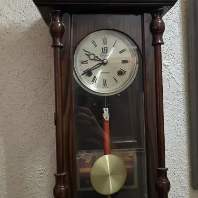 Vintage Unique 31-day regulator wall clock in a dark wood case, featuring an ornate carved pediment with winged horses and a brass pendulum.