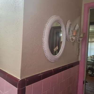 Vintage white hobnail milk glass oval mirror and matching wall sconces, mounted above pink bathroom tiling.