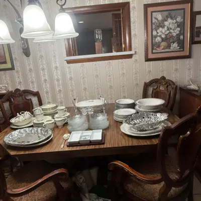 Traditional wooden dining table and chairs set, featuring an assortment of fine china, glassware, and serving platters.
