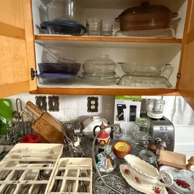 Assorted kitchenware including Pyrex baking dishes, silverware sets in organizers, a knife block, and small appliances displayed on a...