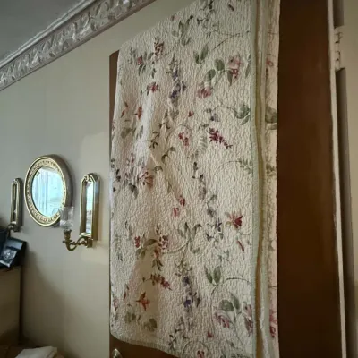 Liz Claiborne floral quilted throw blanket draped over a wooden door, featuring a delicate vine and flower pattern on a cream background.