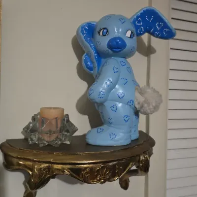 Vintage hand-painted blue ceramic bunny figurine with heart patterns and a fluffy tail, displayed on a small gold-painted ornate wall...