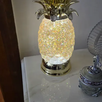 Decorative illuminated pineapple lamp with a gold-finished metal crown and base, featuring a textured, glowing glass body.