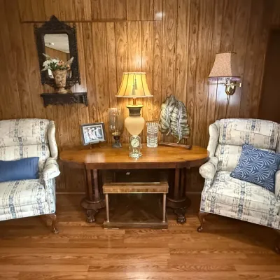 Pair of vintage wingback armchairs with blue and white patterned upholstery, flanking a classic wooden library table with carved legs and...