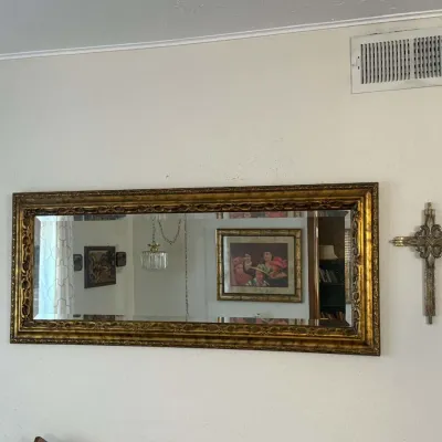 Large horizontal wall mirror with an ornate, gilded frame, flanked by two decorative metal wall crosses.