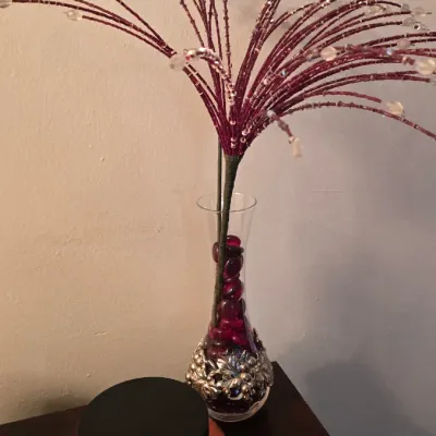 Decorative glass vase with an ornate silver-tone metal base, filled with red glass gems and beaded floral sprays, shown next to a large...